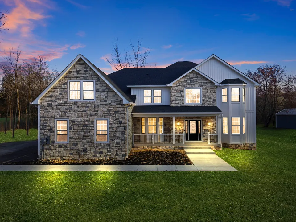 Two-story home with a stone front and white board-and-batten siding, lit up at dusk