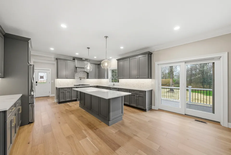 Kitchen with gray shaker cabinets, a white quartz island and sliding doors to the deck