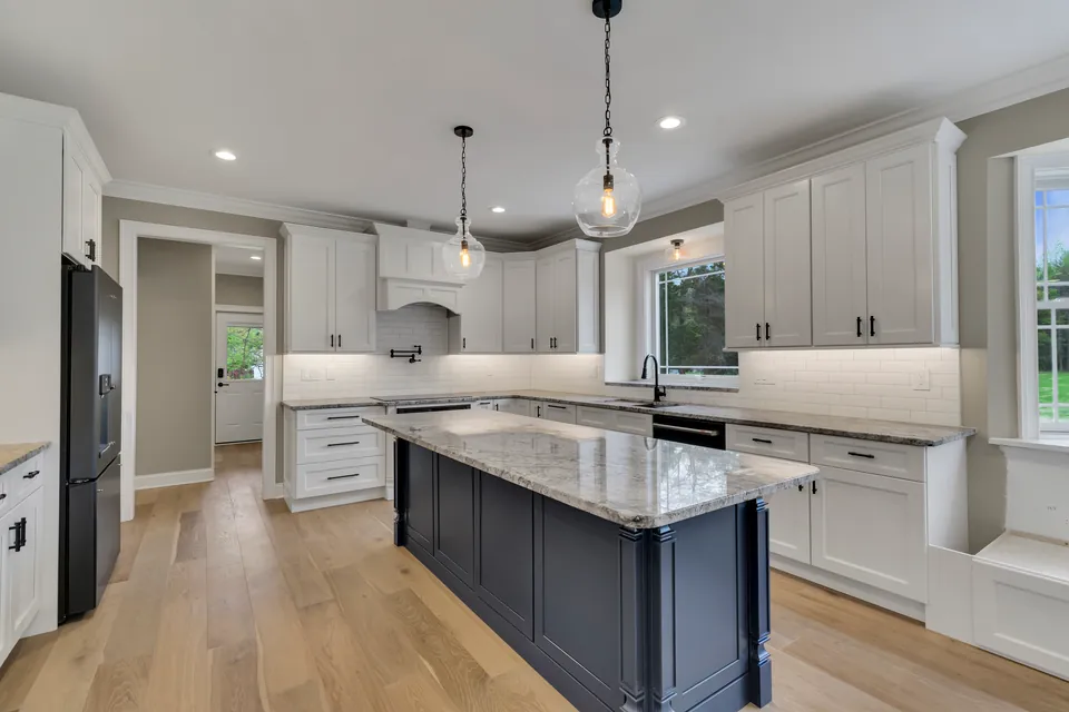 Kitchen with white shaker cabinets, a navy island with a granite top and glass pendant lights