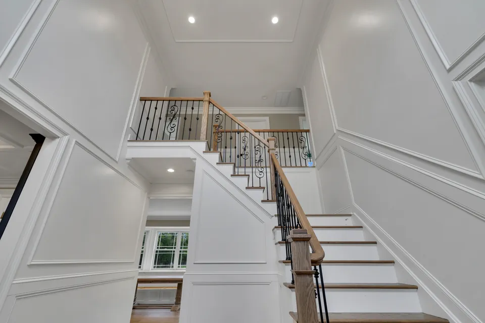 Two-story foyer with panel moulding and an oak staircase with scrolled iron balusters