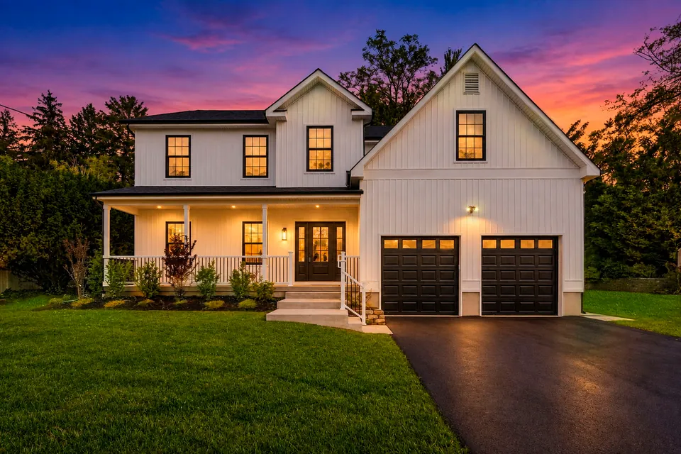 White farmhouse-style home with a covered front porch and two-car garage, lit up at dusk