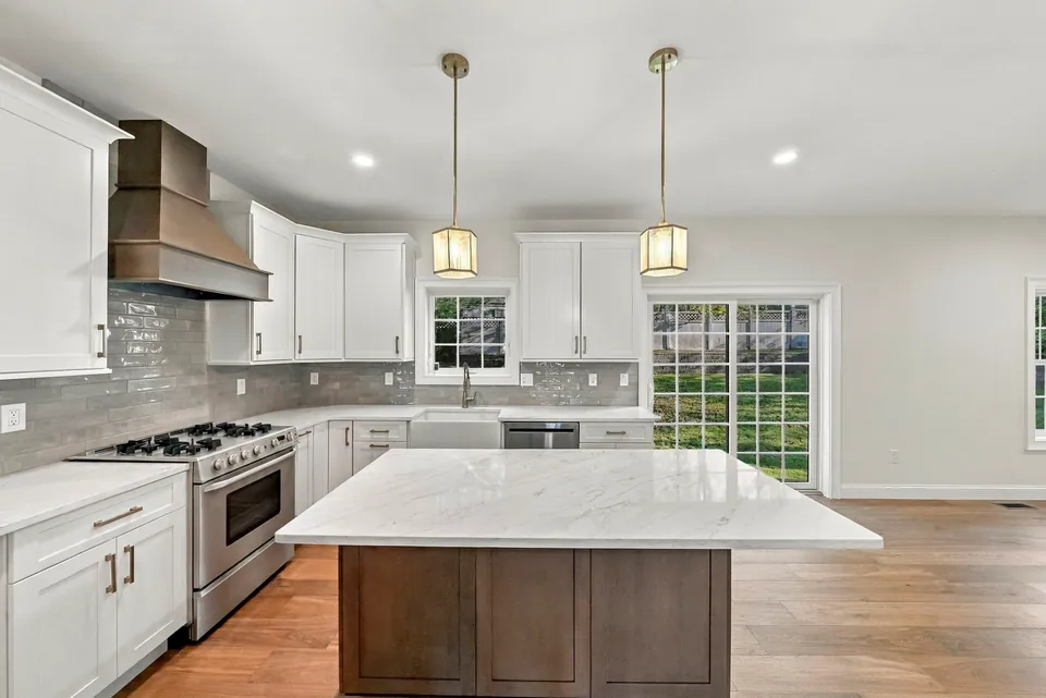 Kitchen with white shaker cabinets, a range hood, a marble-look island and a farmhouse sink