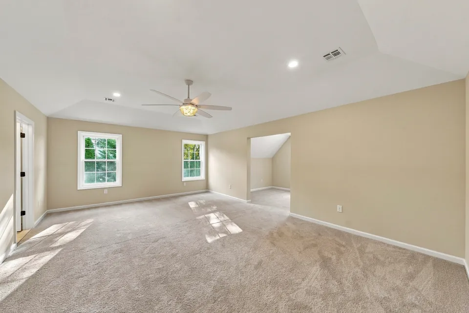Large carpeted bedroom with a tray ceiling and ceiling fan